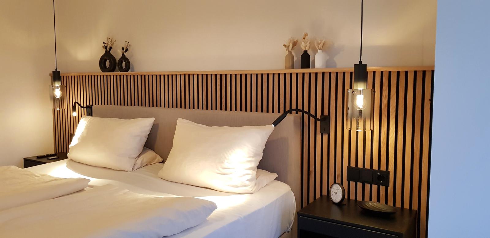 Schlafzimmer mit Bett, Holzpaneelen und Nachttischen mit Lampen.