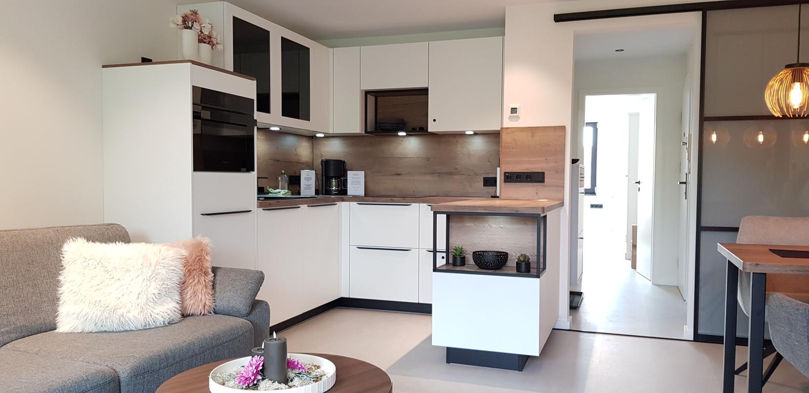 Wohnküche mit Sofa, Küchenzeile und Essbereich. Moderne Einrichtung mit Holz- und Metallakzenten.