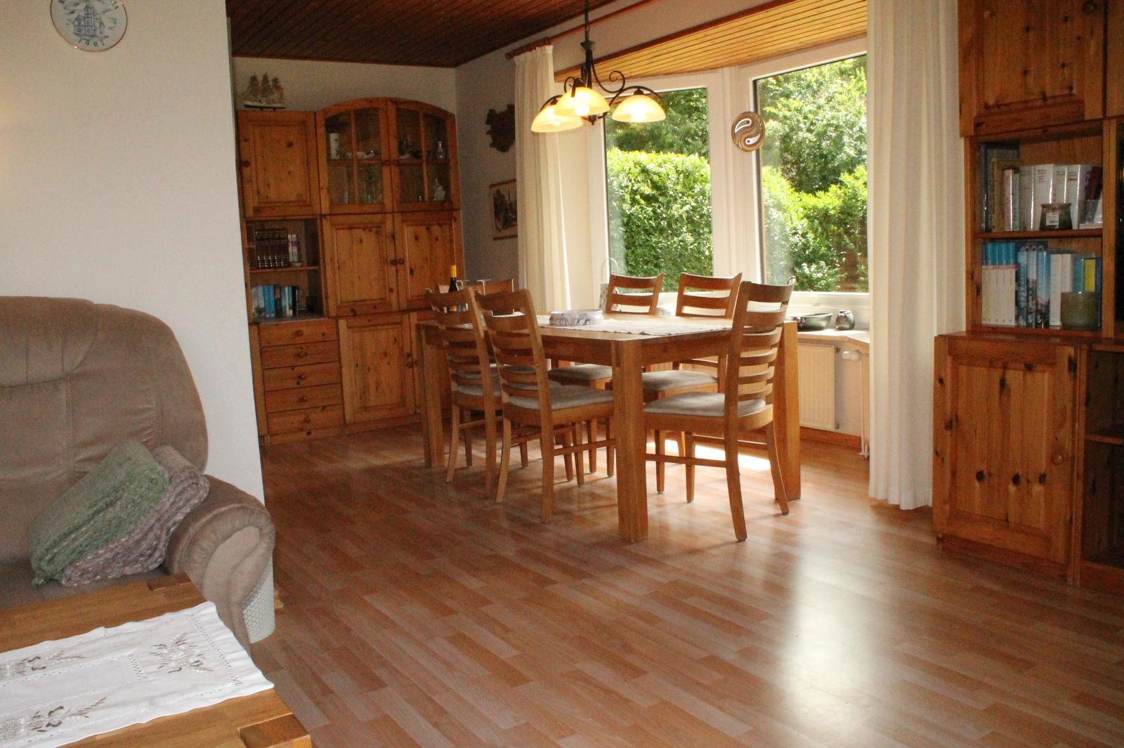 Esszimmer mit Holztisch, Stühlen und Bücherregalen. Holzfußboden und Fenster mit Blick auf Garten.