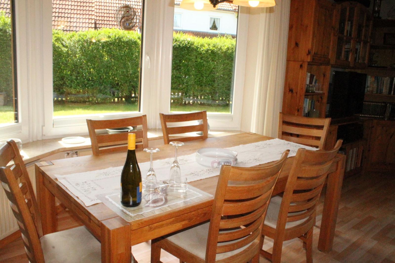 Holztisch mit Stühlen und Weinflasche vor Fenster mit Blick auf Garten