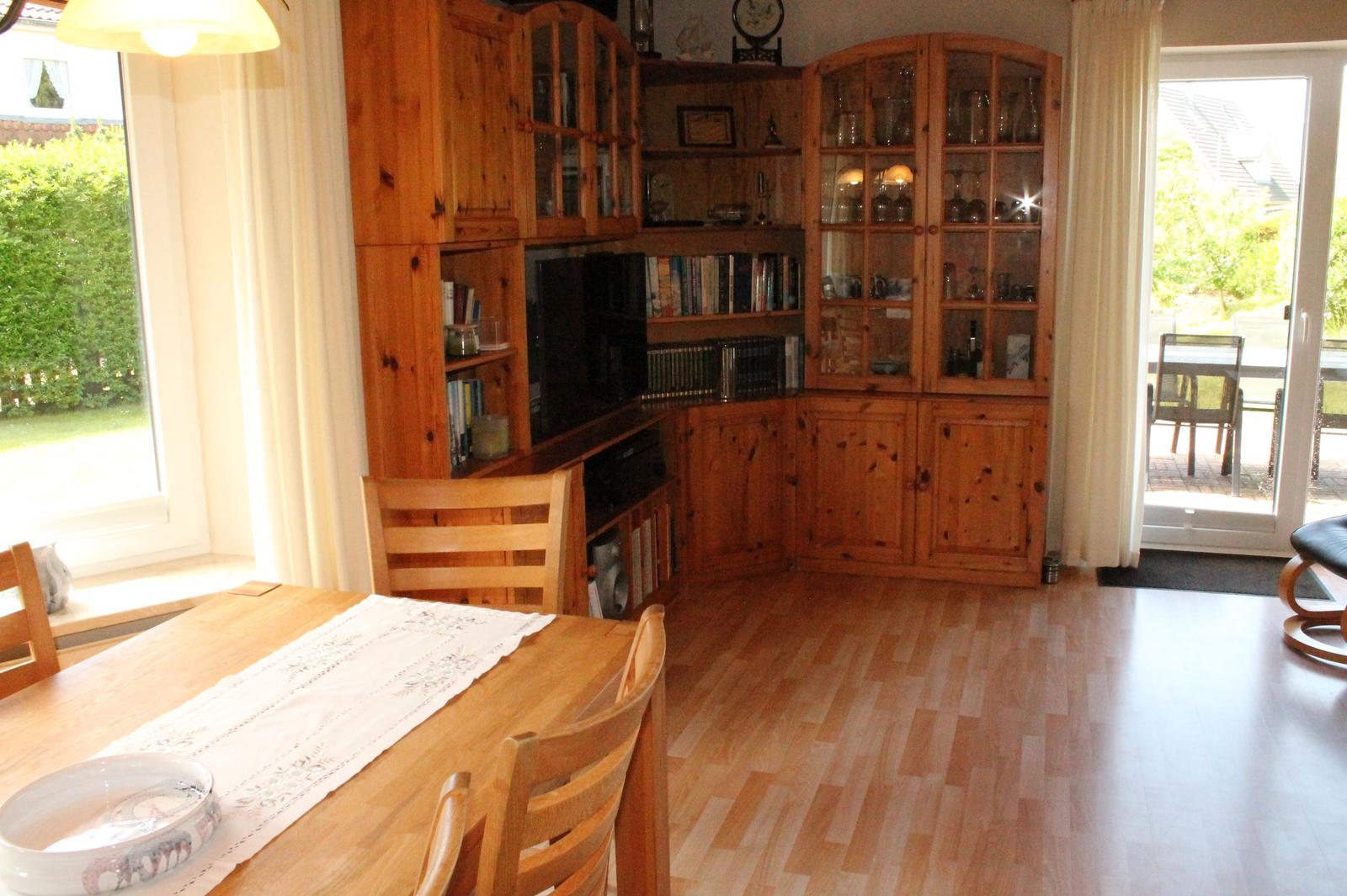 Esszimmer mit Holztisch, Stühlen und Bücherregal. Durchgang zur Terrasse.