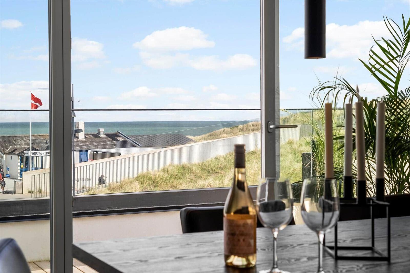Tisch mit Weinflasche und Gläsern vor großem Fenster mit Meerblick.