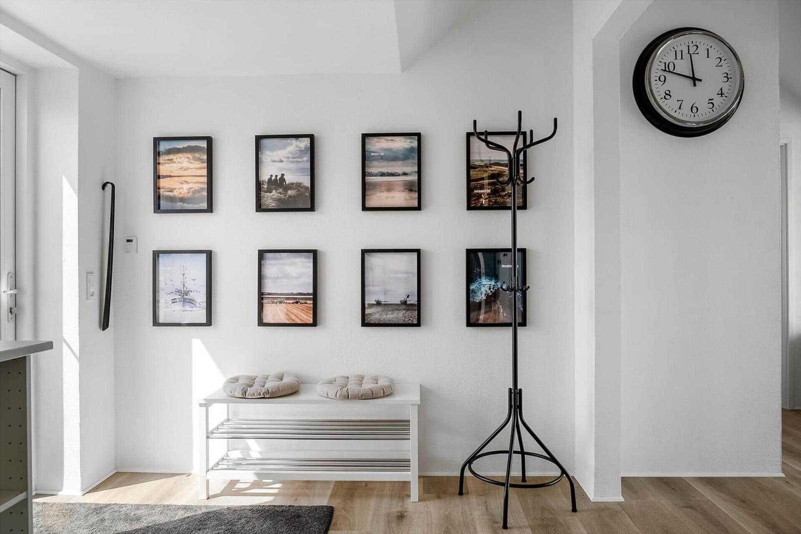 Eingangsbereich mit Bildern an der Wand, Hocker, Kleiderständer und Wanduhr.