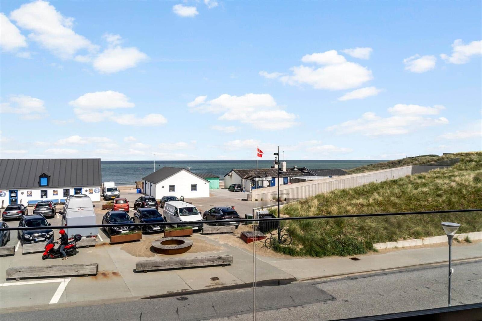 Parkplatz mit Gebäuden und Strand im Hintergrund unter blauem Himmel.