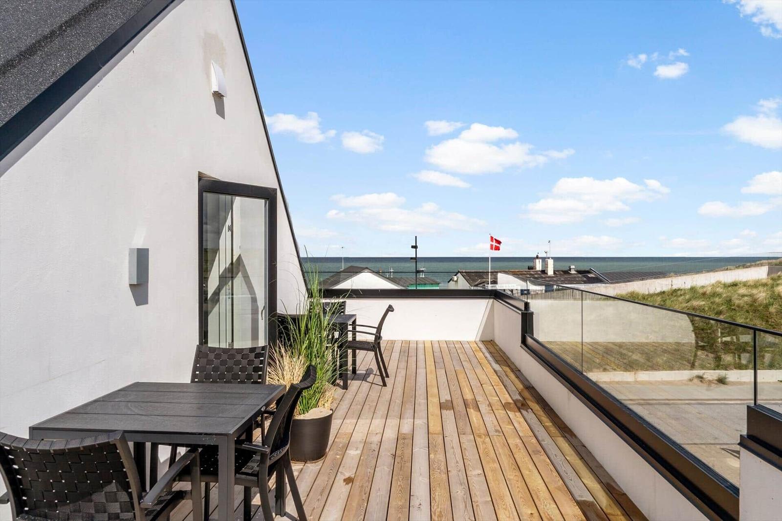 Terrasse mit Tisch und Stühlen, Blick auf Meer und Strand.