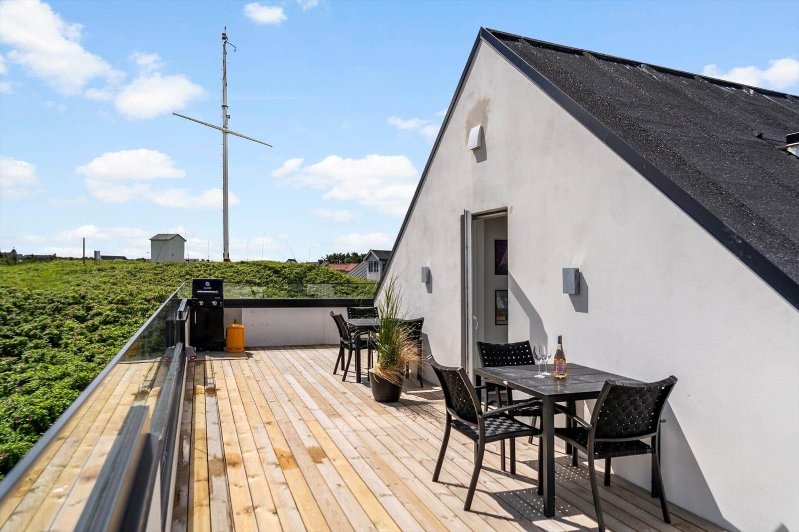 Terrasse mit Tisch, Stühlen und Grill. Blick auf grüne Fläche und Mast.