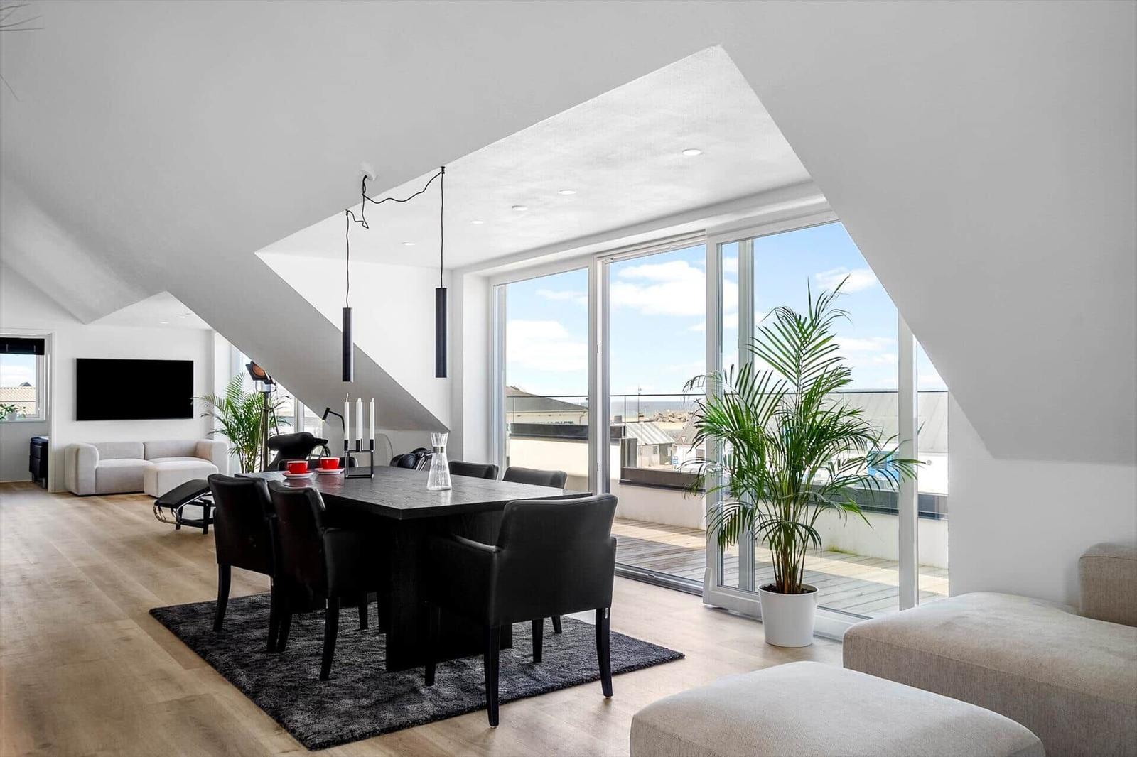 Essbereich mit Tisch und Stühlen, große Fenster mit Balkonblick, Zimmer mit Fernseher und Sofa.