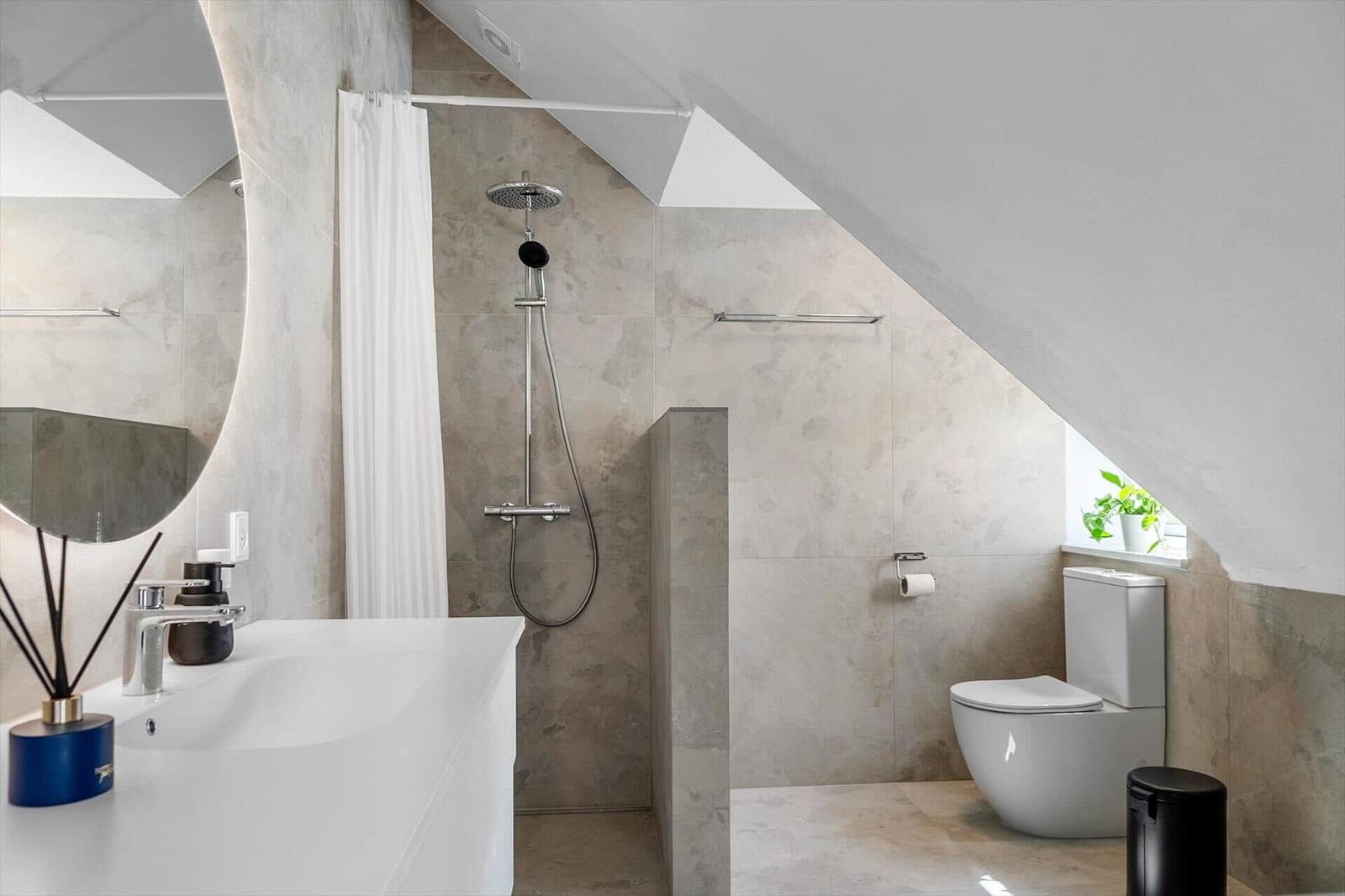 Badezimmer mit Dusche, WC und Waschtisch unter schrägen Dachbalken.