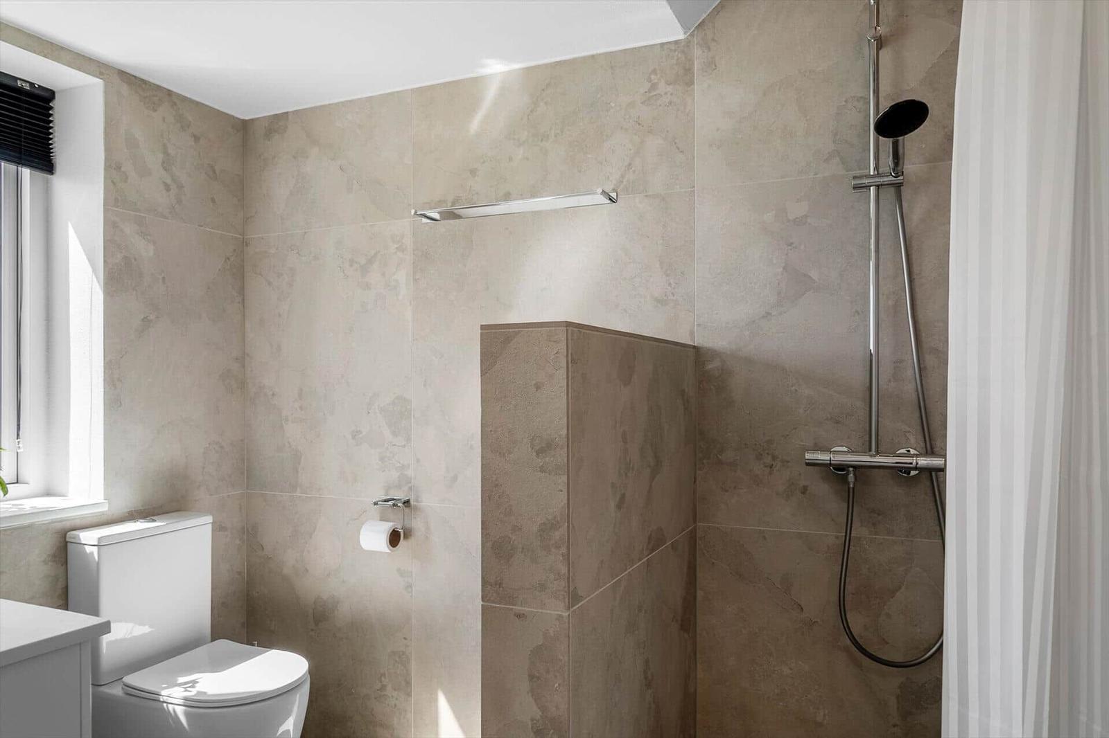 Badezimmer mit Dusche, Toilette und Fenster