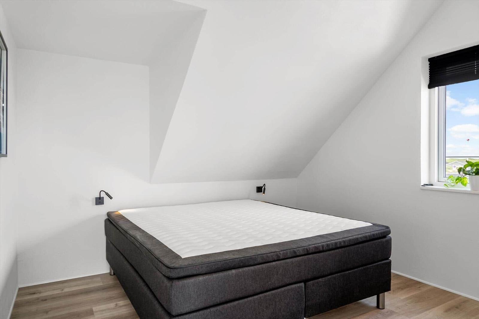 Schlafzimmer mit Doppelbett, Holzboden und Dachschrägen. Fenster mit Pflanze.
