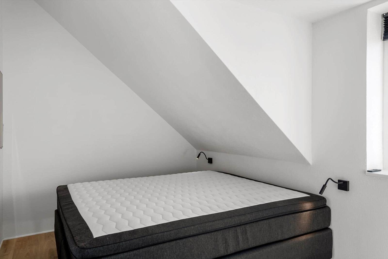 Schlafzimmer mit Dachschrägen, weißer Matratze und schwarzem Bettgestell.