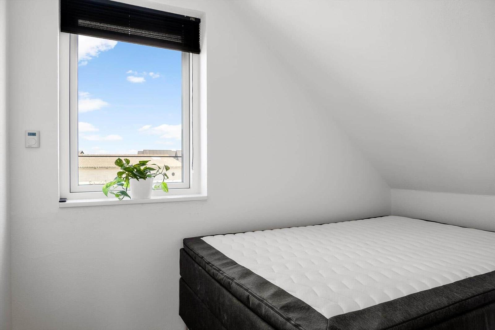 Schlafzimmer mit Dachschrägen, Bett und Fenster mit Pflanze.