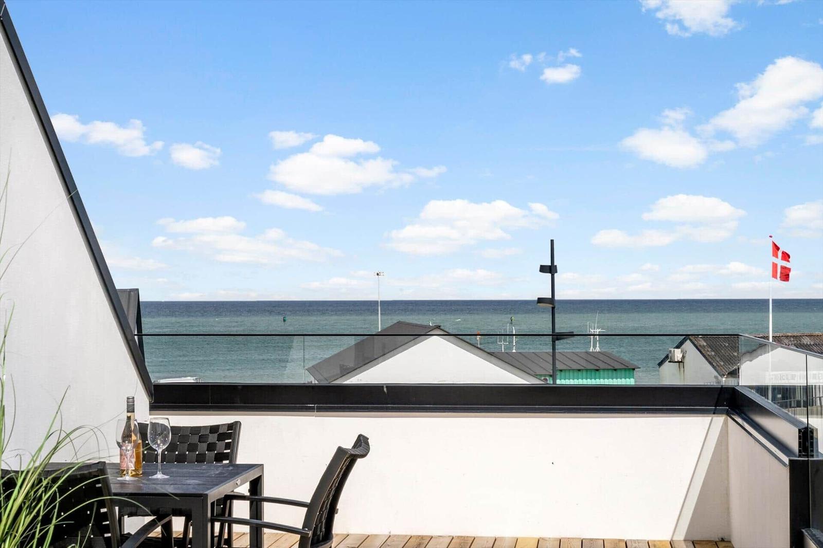 Terrasse mit Tisch und Stühlen, Blick auf Meer und Dänemarkflagge.