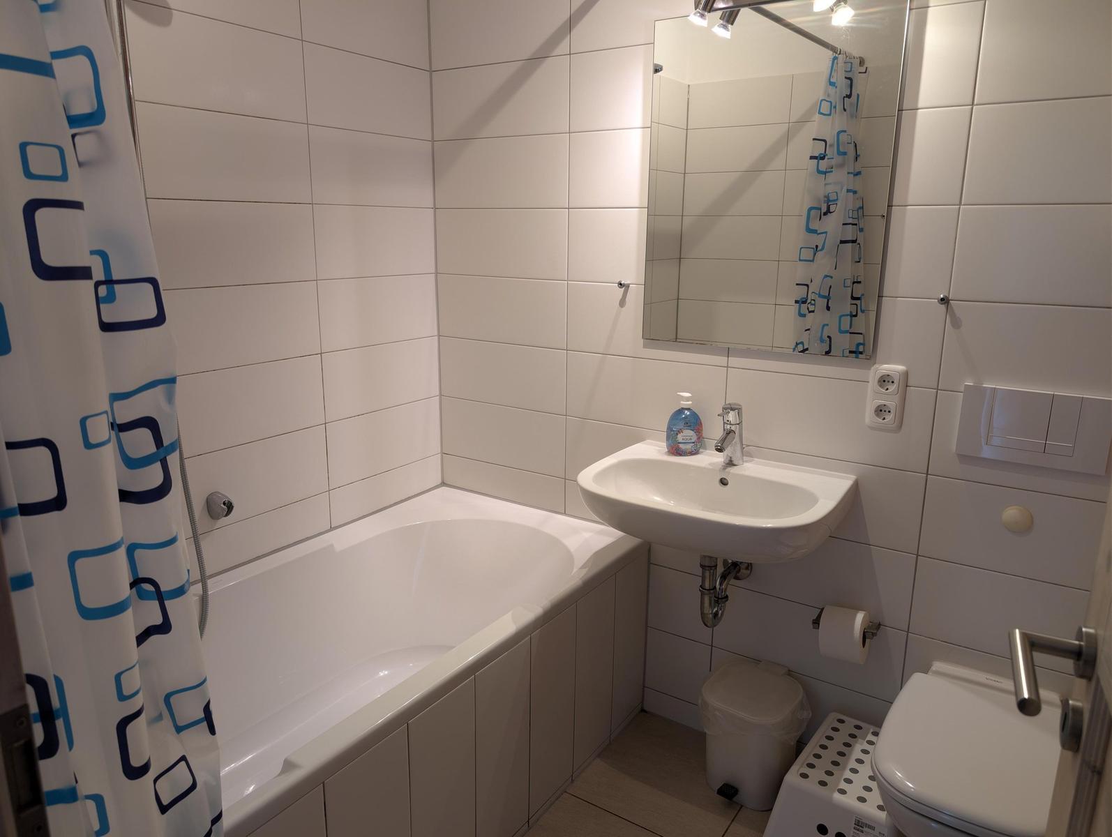 Badezimmer mit Badewanne, Spiegel, Waschbecken und Toilette.