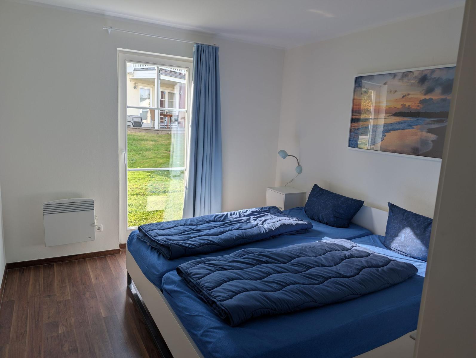 Schlafzimmer mit Doppelbett, Fenster zur Terrasse und Wandbild.