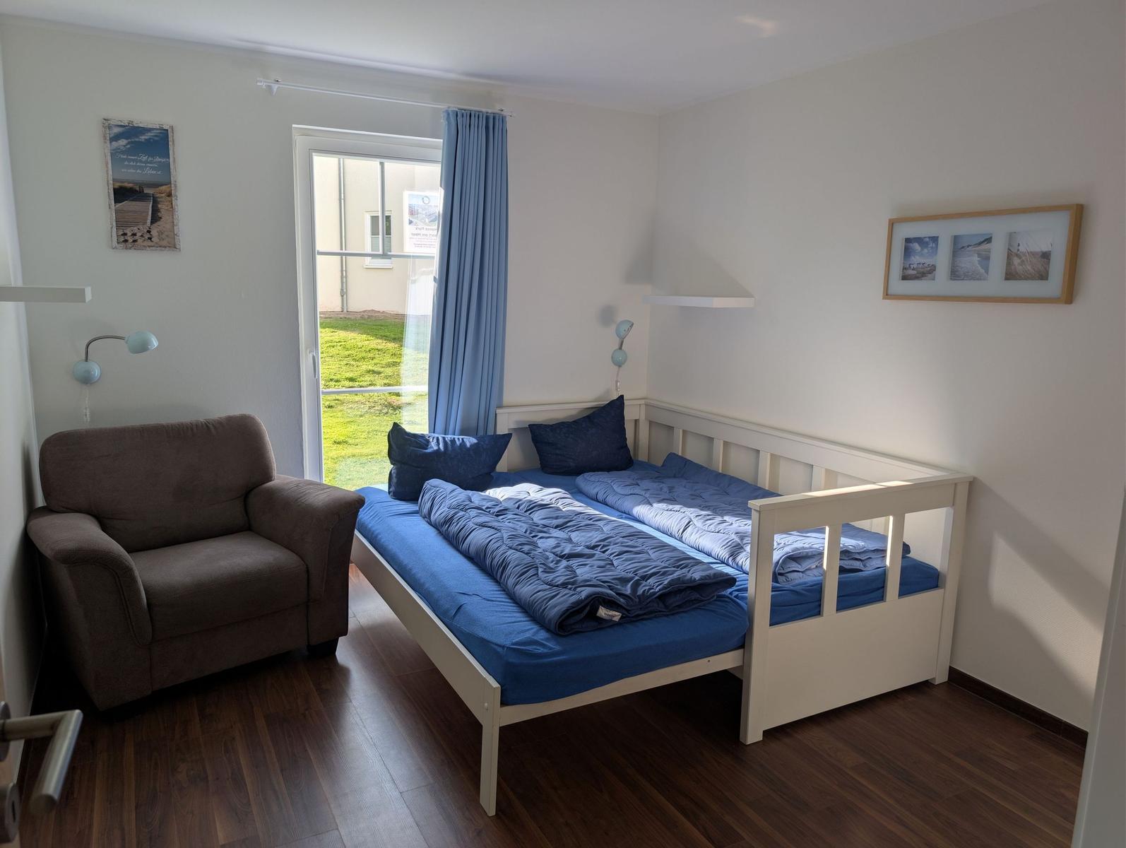 Schlafzimmer mit Bett, Sessel und Glastür zum Garten.