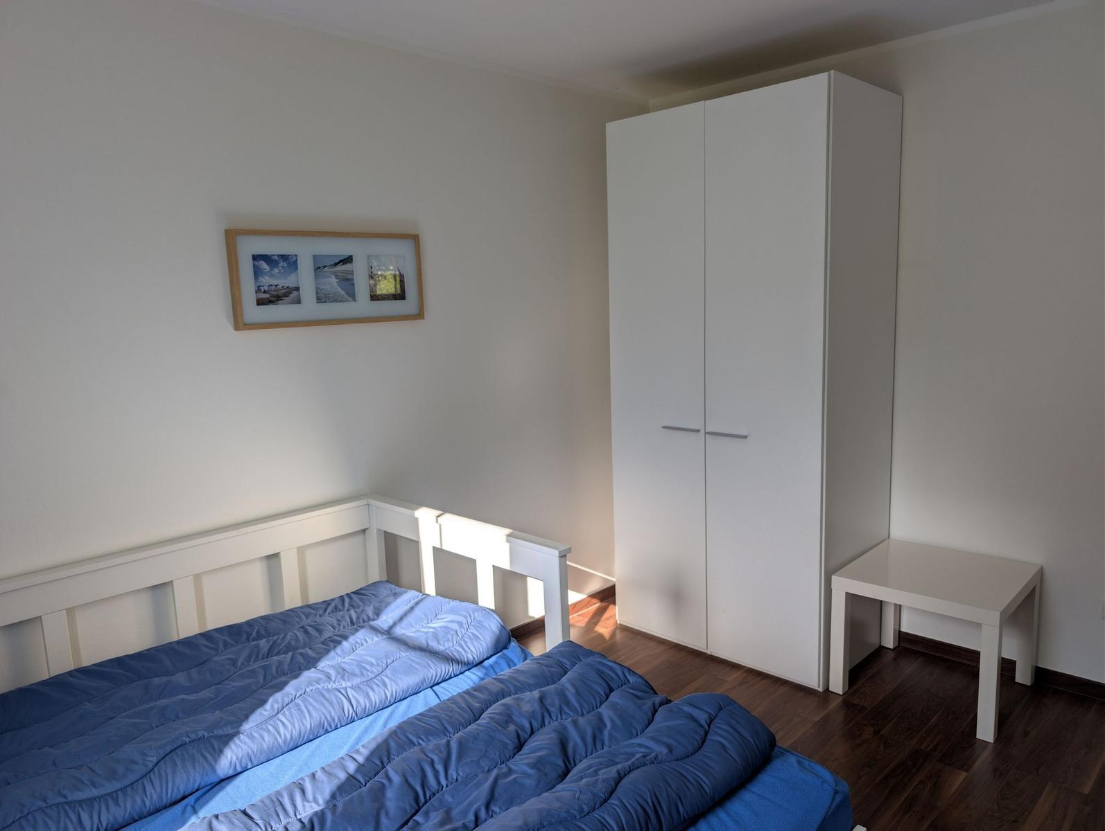 Schlafzimmer mit Bett, Kleiderschrank und Tisch. Wandbild mit Strandmotiven.