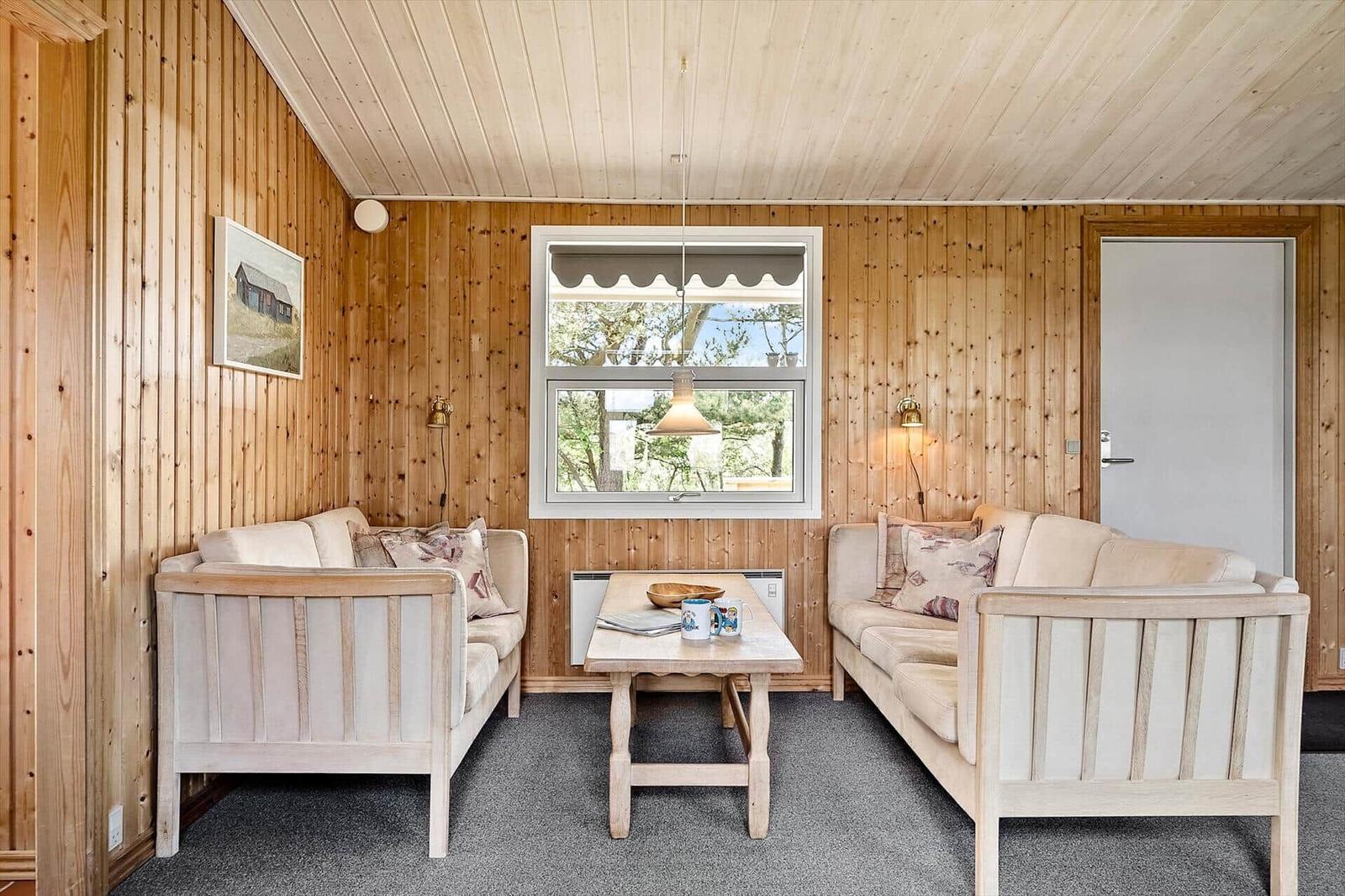 Wohnzimmer mit Holzwänden, zwei Sofas und Tisch. Fenster zeigt Außenansicht.
