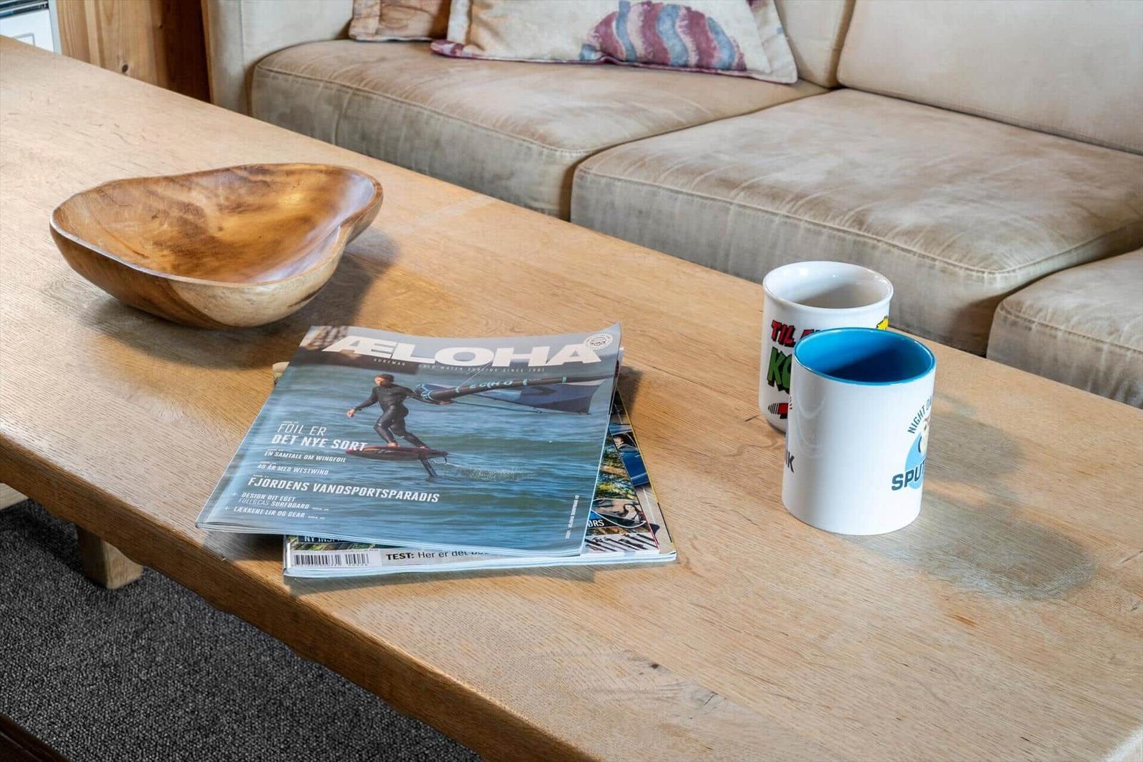 Holztisch mit Zeitschrift, Schale und Tassen vor einem Sofa.