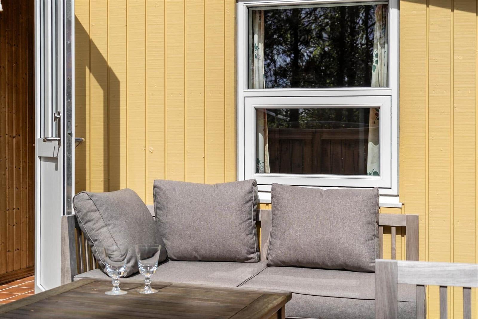 Terrasse mit Sitzbank, Tisch und Gläsern vor gelbem Haus mit Fenster.