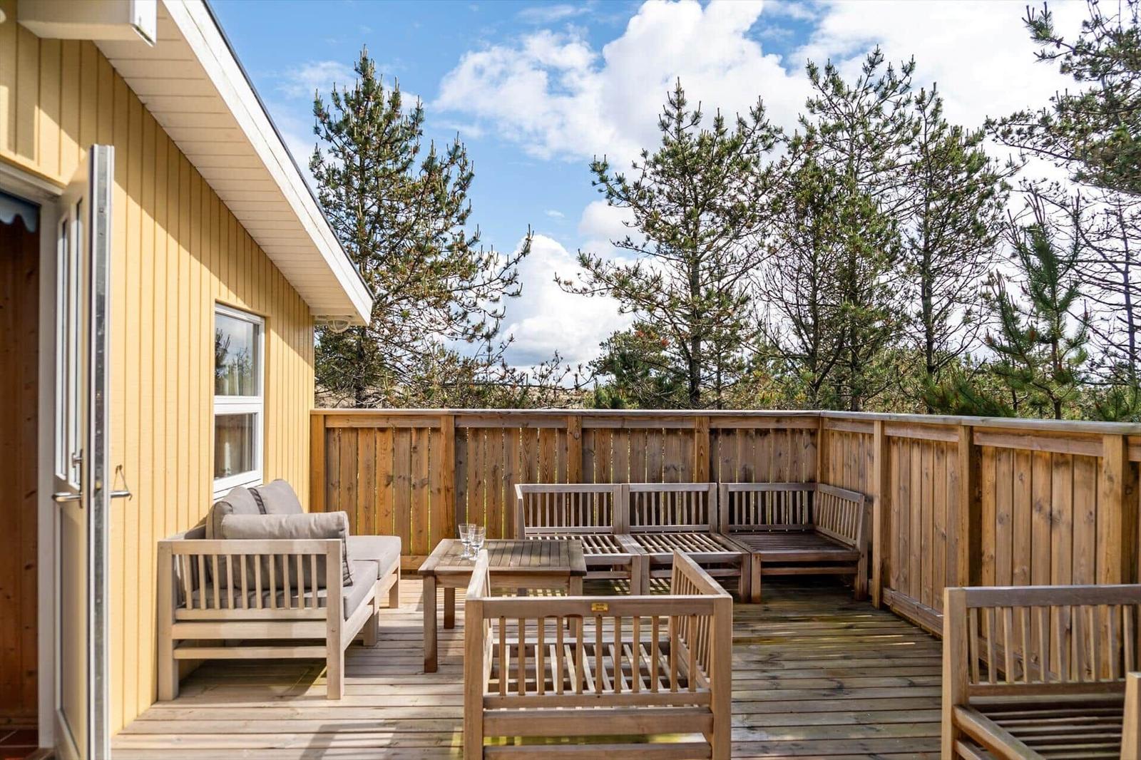 Terrasse mit Holzmöbeln und Blick auf Bäume unter blauem Himmel.