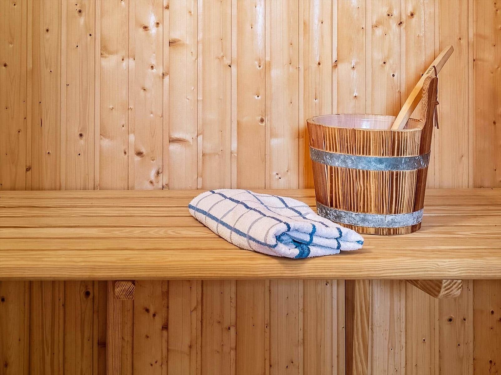 Holzbank in Sauna mit Handtuch und Eimer mit Besen.