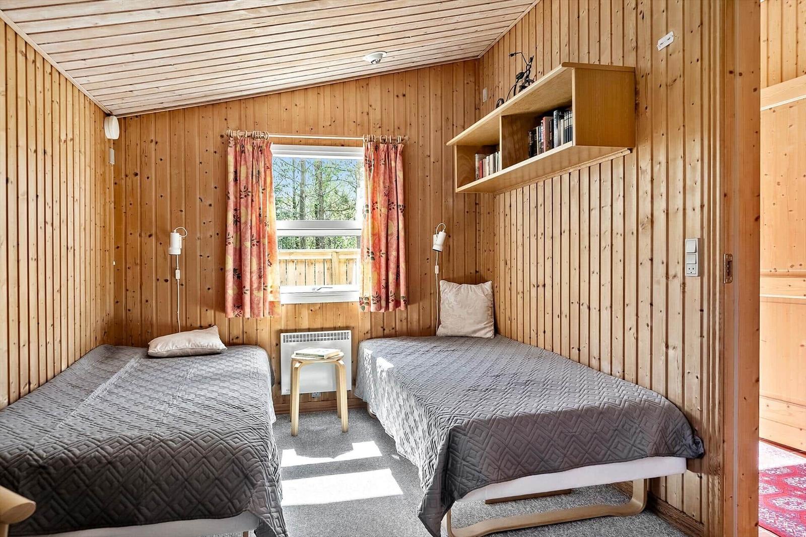 Zwei Einzelbetten in einem holzverkleideten Raum mit Fenster und Bücherregal.