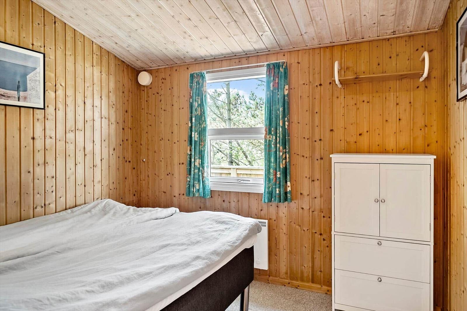 Schlafzimmer mit Holzwand, Bett, Fenster und Schrank.