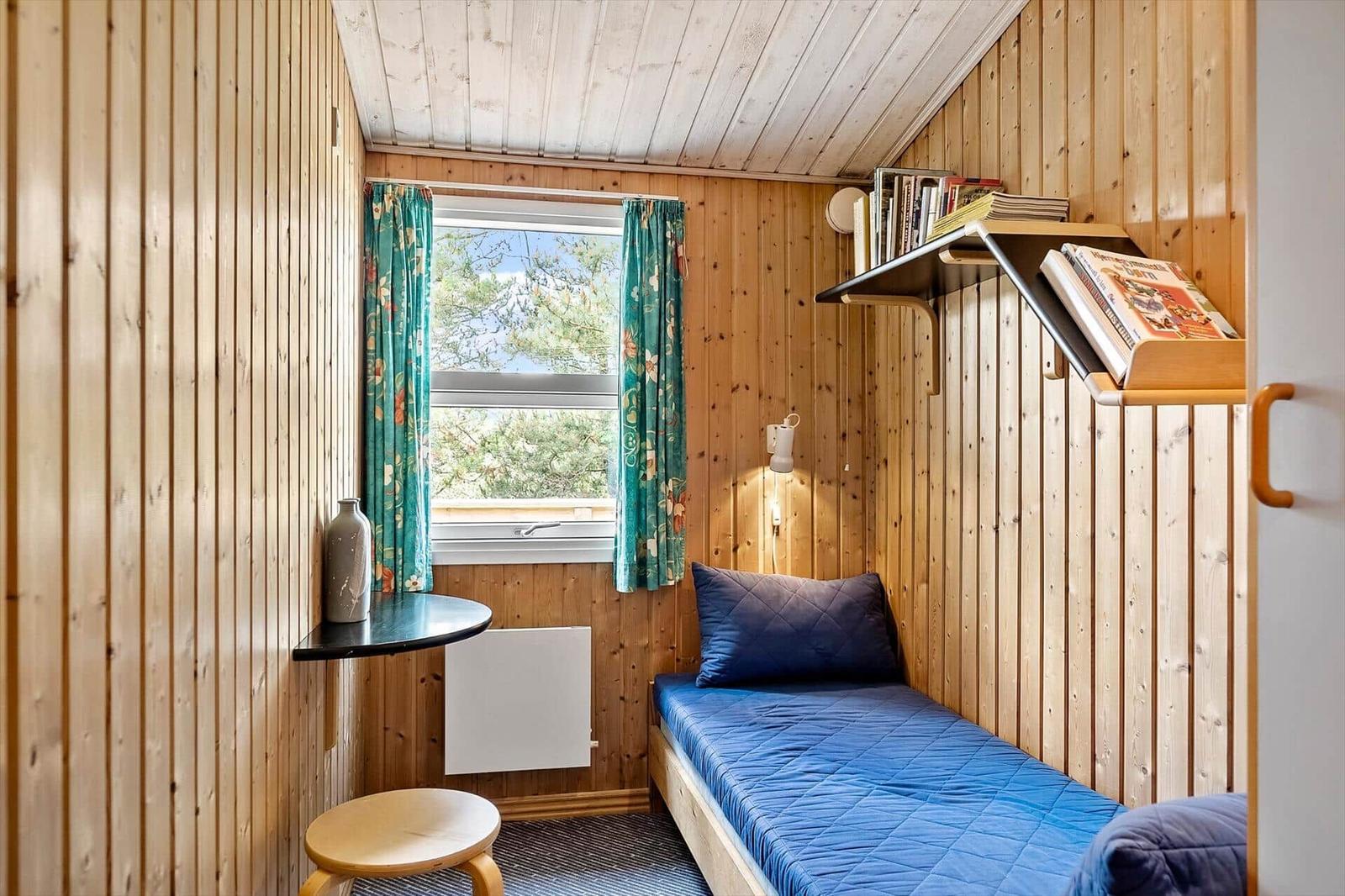 Schlafzimmer mit Bett, Fenster, Regal und Tisch.