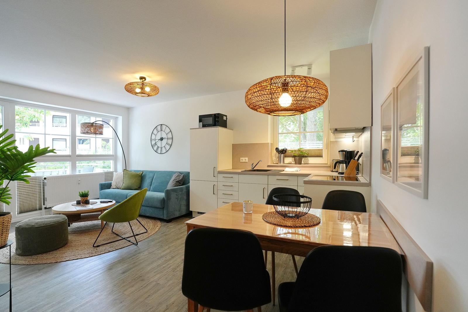 Wohn- und Küchenbereich mit Sofa, Esstisch und Fenstern.