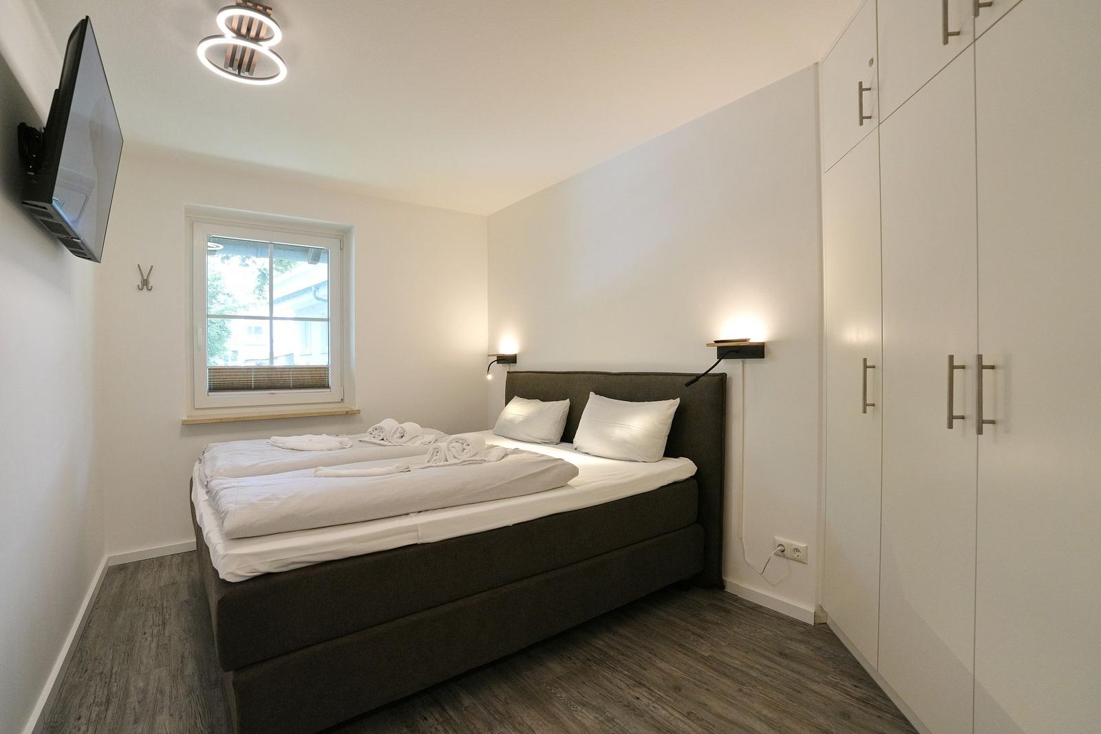 Schlafzimmer mit Bett, Fenster, Kleiderschrank und Wand-TV.