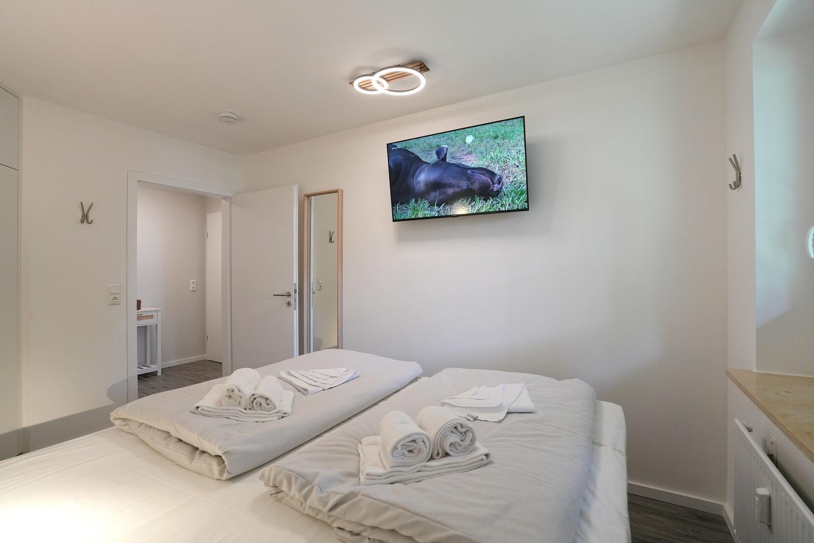 Zwei Betten mit weißen Bettwäsche und Handtüchern. Wandfernseher und Tür zum Bad.