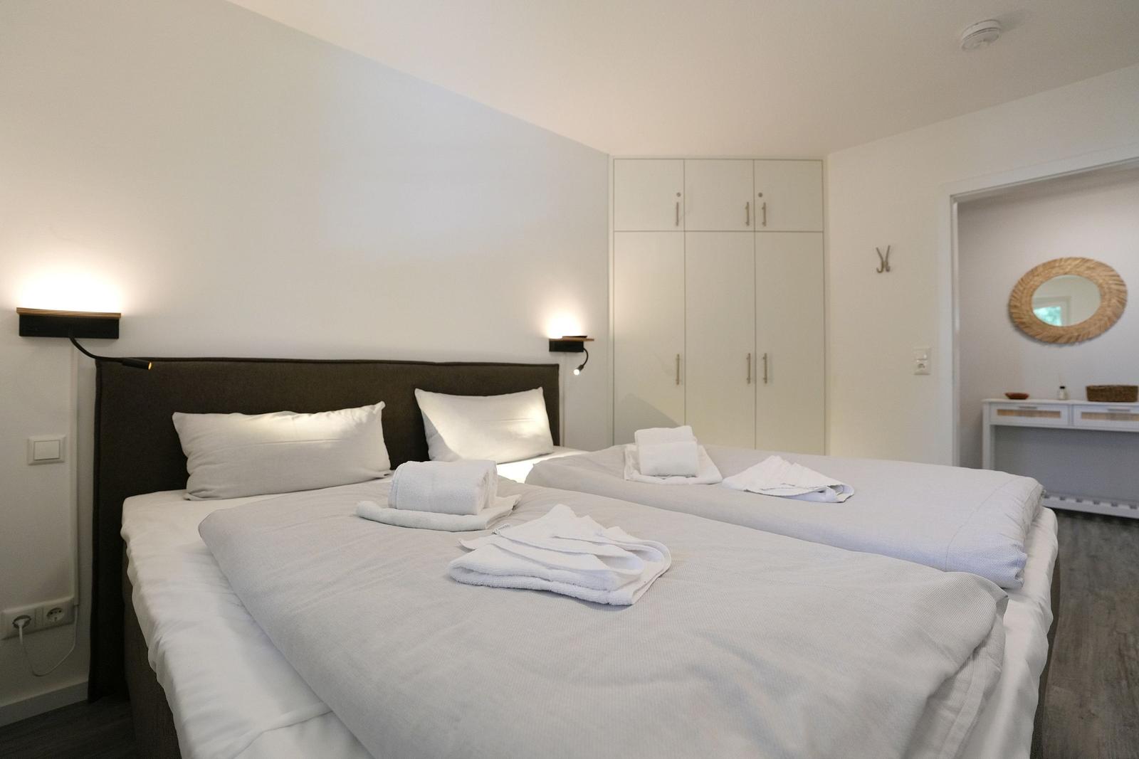 Zwei Betten mit weißen Laken und Handtüchern. Hintergrund: Schrank und Spiegel.