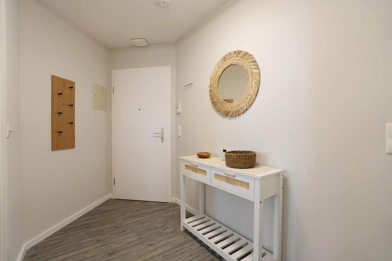 Eingangsbereich mit weißem Tisch, runden Spiegel und Holzgarderobe an der Wand.