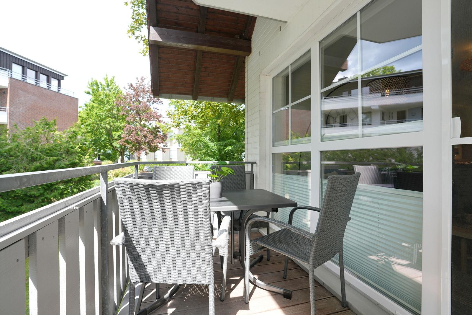 Terrasse mit Tisch und Stühlen, Blick auf Bäume und Gebäude.