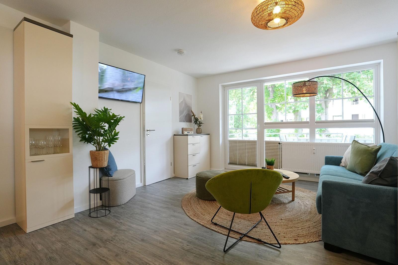 Wohnzimmer mit Sofa, grüner Sessel, TV und großem Fenster.