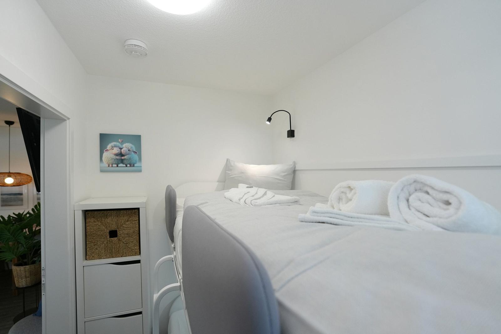 Ein Schlafzimmer mit Bett, Nachttisch und Wandbild. Handtuch und Kissen sind auf dem Bett.