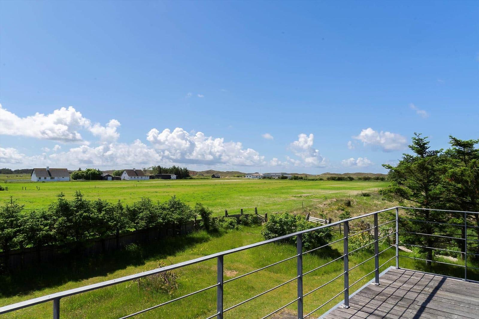 Terrasse mit Blick auf grünes Feld und Häuser unter blauem Himmel.