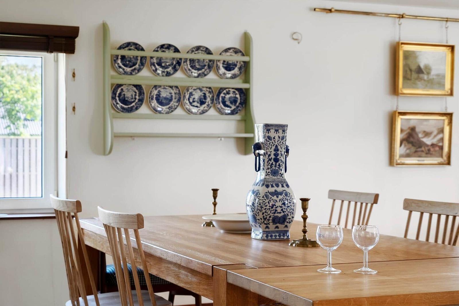 Esszimmer mit Holztisch, Stühlen und blau-weißen Porzellanplatten an der Wand.