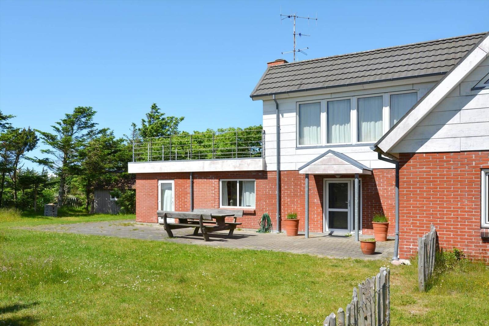 Haus mit Terrasse, Grillplatz und Garten. Roter Backsteinbau mit weißen Fenstern.