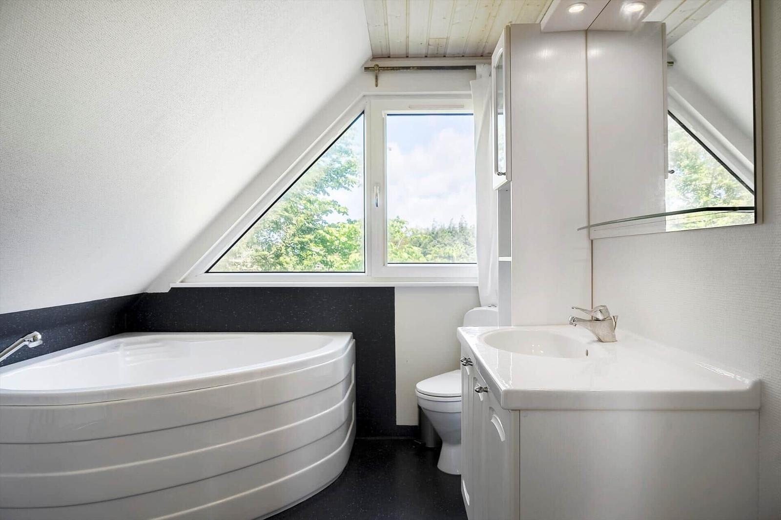 Badezimmer mit Dusche, Badewanne und Fenster. Dachgeschoss mit schräger Decke.