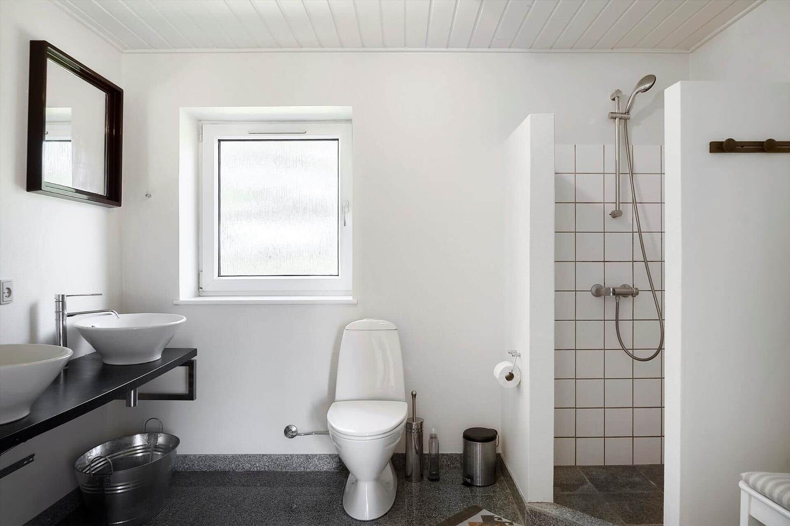 Badezimmer mit Dusche, Toilette und Waschbecken. Fenster und Spiegel sichtbar.