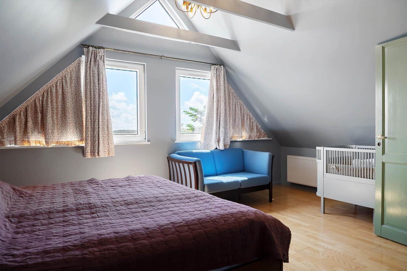Schlafzimmer mit Dachfenster, Bett, Sofa und Kinderbett.