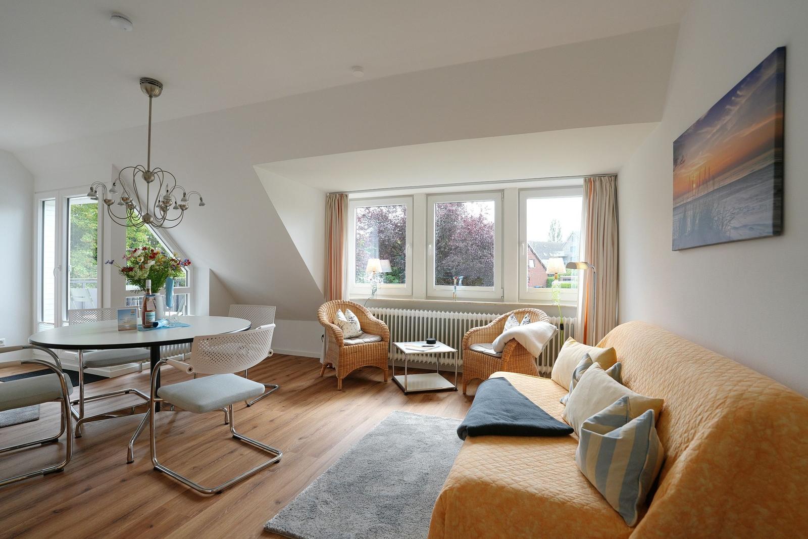 Wohn- und Essbereich mit Sofa, Stühlen und Fenstern. Holzboden und Deckenlicht.