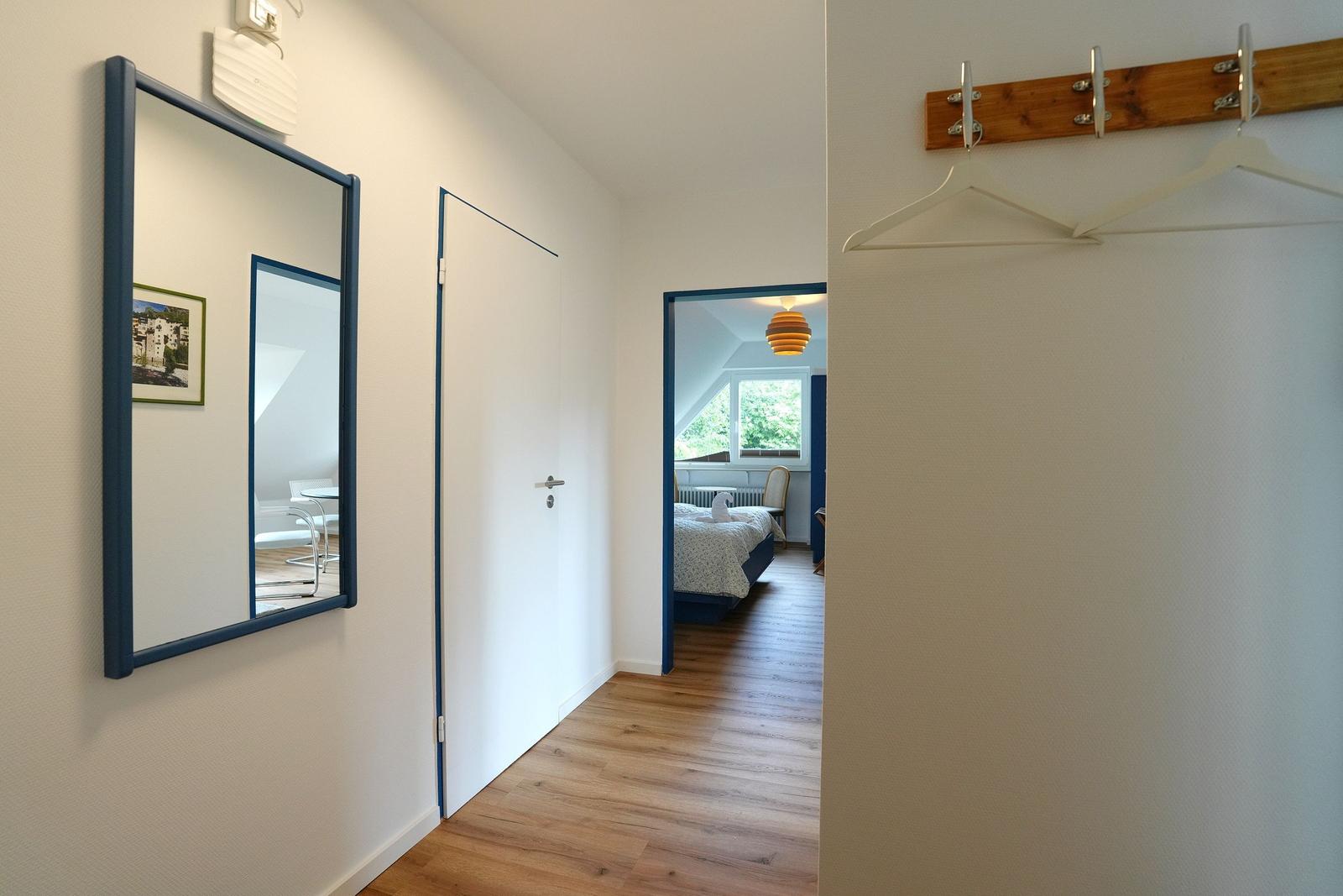 Flur mit Spiegel, Kleiderhaken und Blick in Schlafzimmer mit Bett und Fenster.