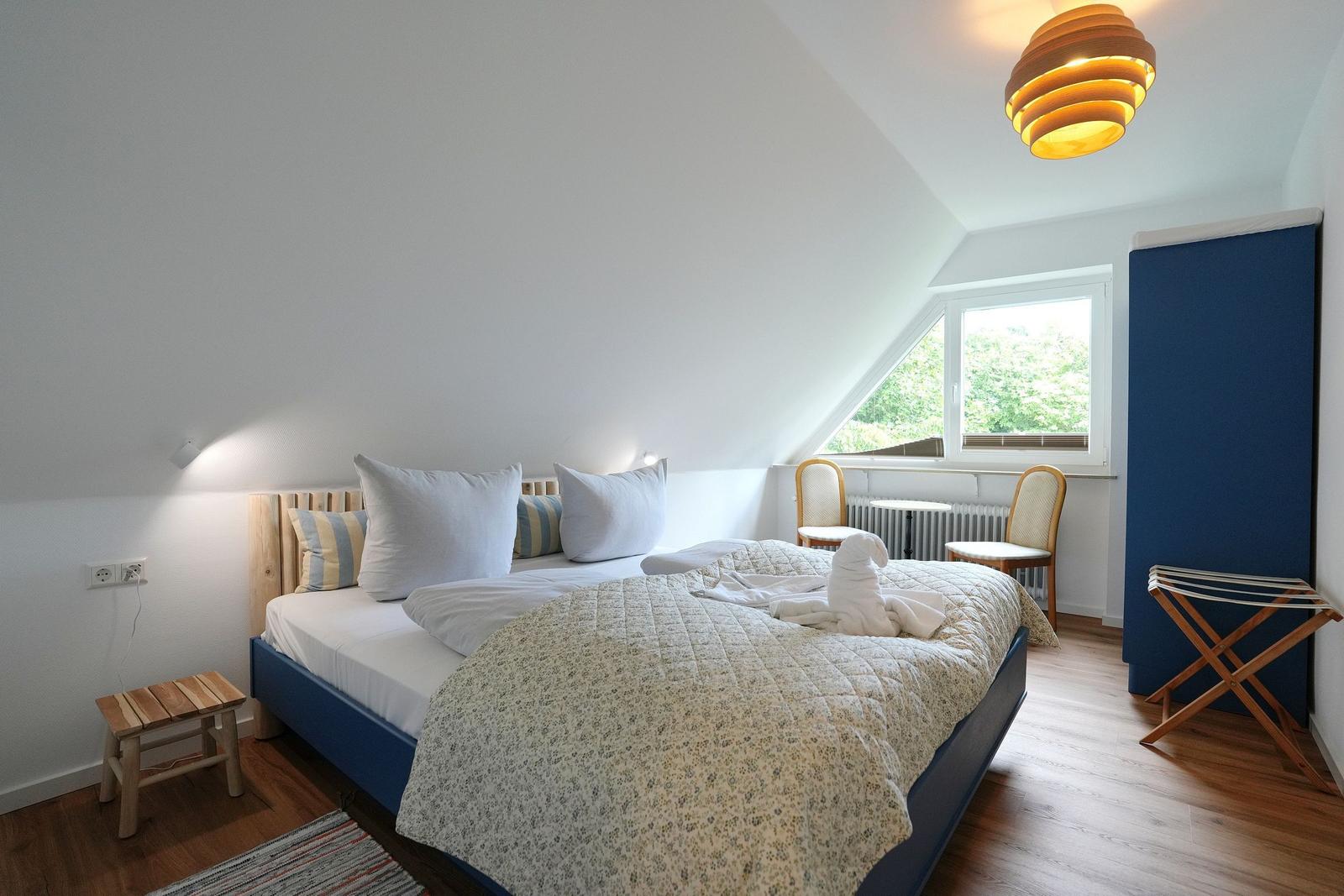 Schlafzimmer mit Dachschrägen, Bett, Fenster und Holzboden.