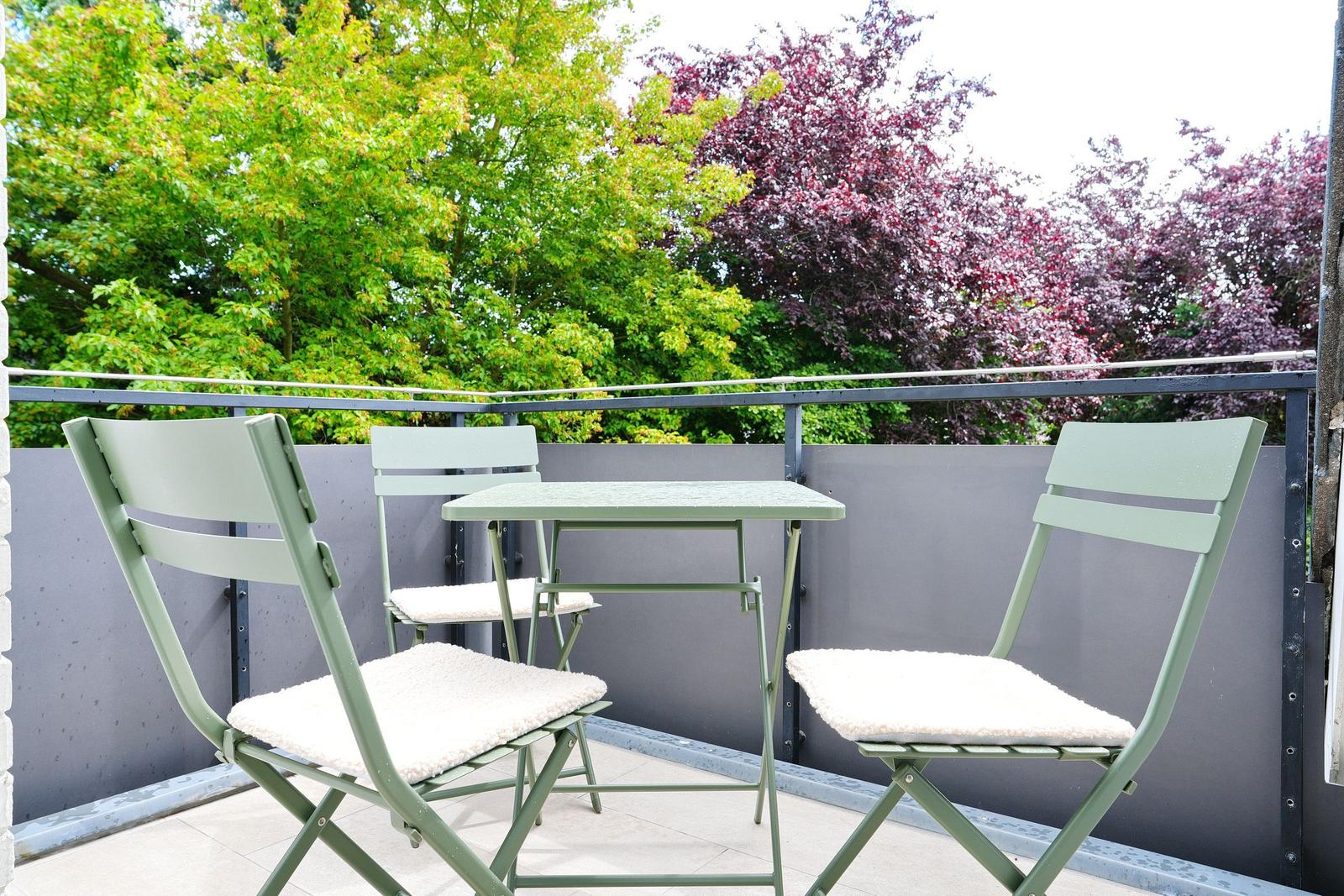 Terrasse mit grünem Tisch und drei Stühlen, Blick auf Bäume.