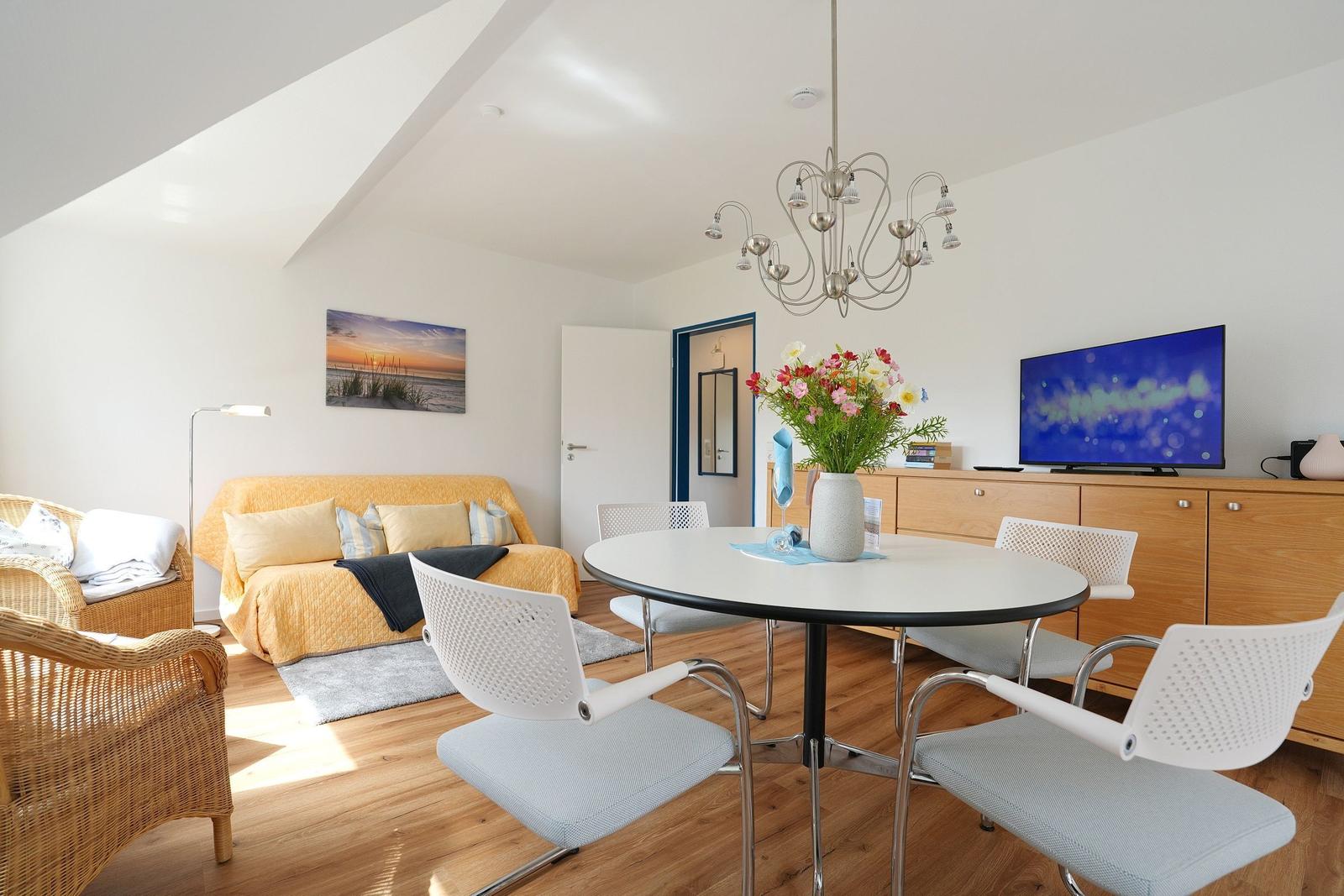 Wohn- und Essbereich mit runden Tisch, weißen Stühlen und gelbem Sofa unter schrägen Decken.