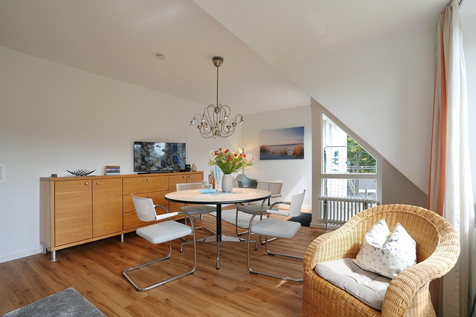 Esszimmer mit runden Tisch, Stühlen und TV. Wohnbereich mit Rattan-Sessel und Fenster.