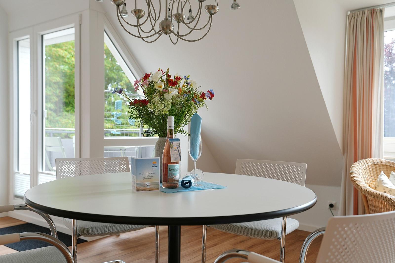Runder Tisch mit Stühlen, Blumen und Wein im Esszimmer mit Blick auf Balkon.